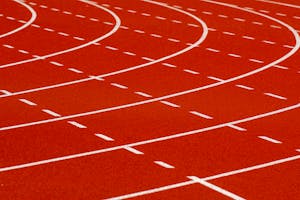 Close-up view of a curved red running track with dashed white lines for athletic sports.